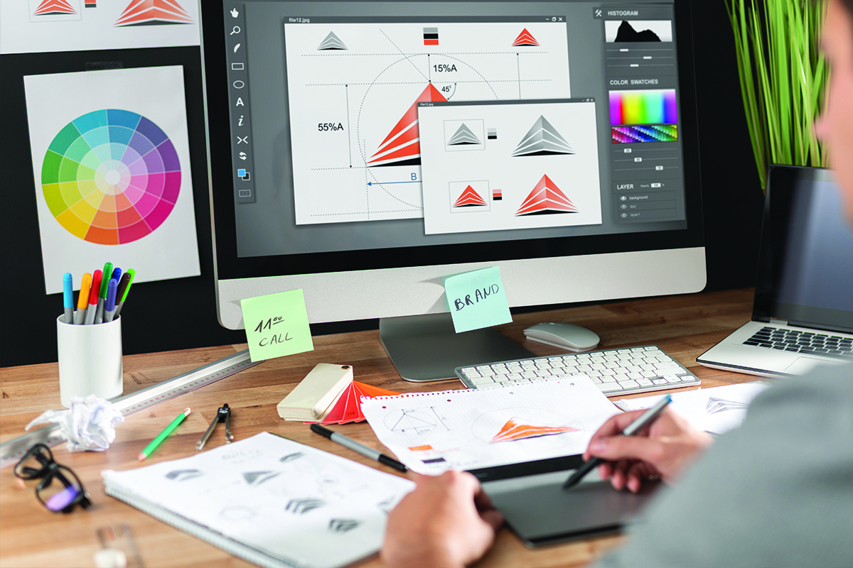 A graphic designer sits at their desk and works on branding concepts on their computer