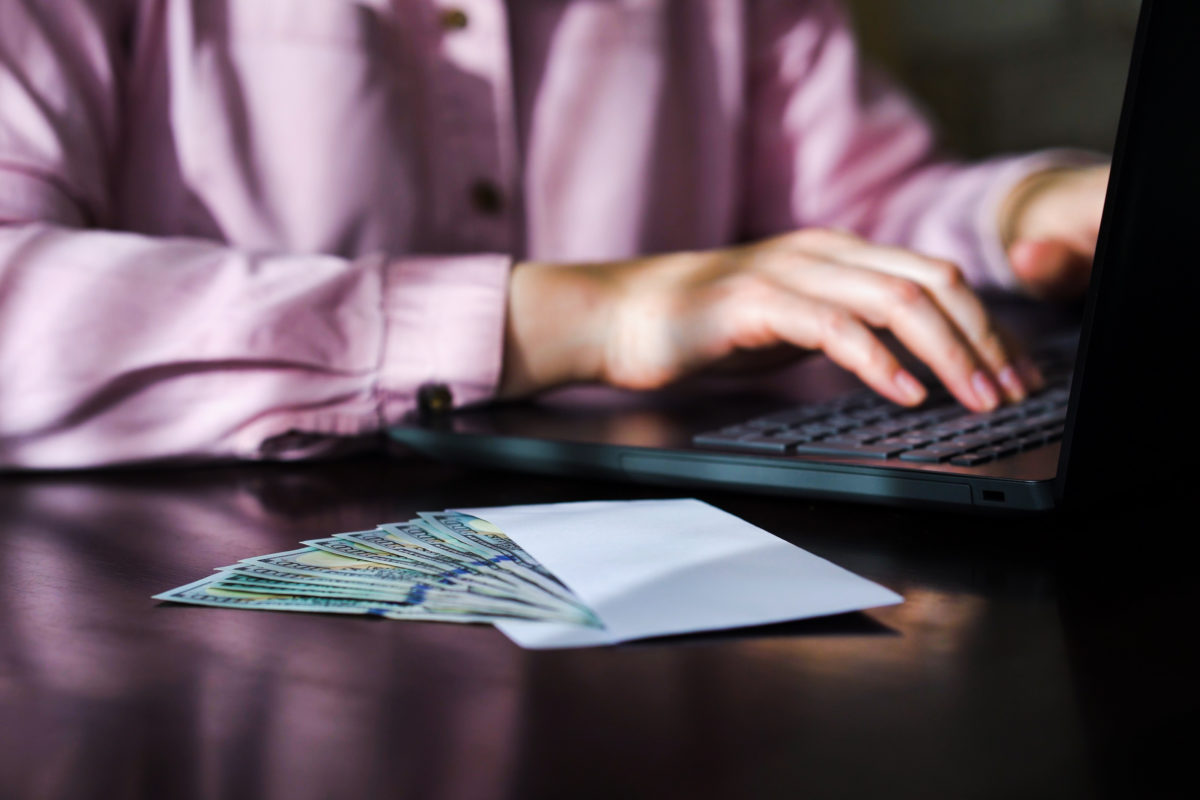 A female office worker types at her laptop with an envelope of money next to her