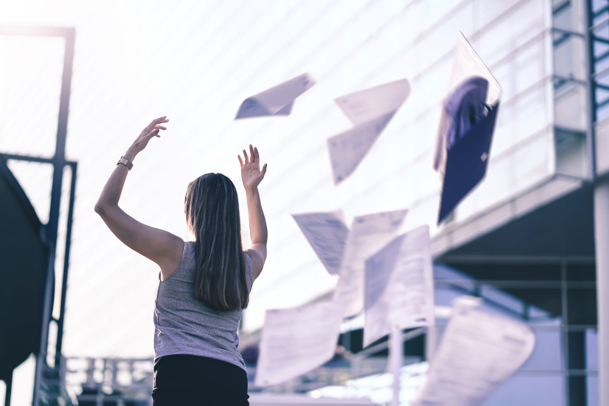 A businesswoman joyously throws paperwork up and behind her as she leaves her job.