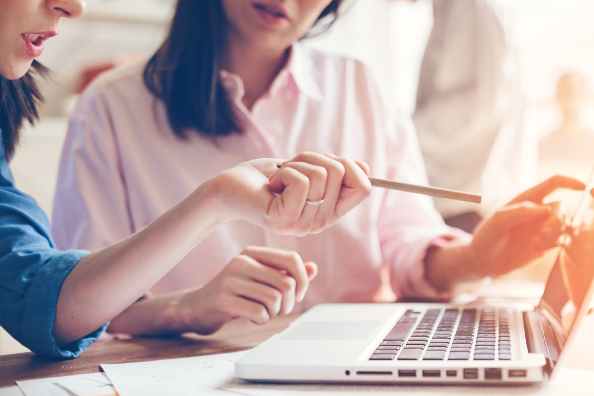 Two businesswomen sit at a laptop, discussing strategies and growth